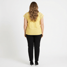 woman facing a white background wearing a yellow shirt with black pants
