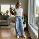 Woman standing in a living room wearing a white t-shirt and blue jeans.