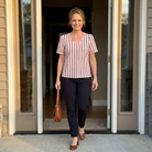 Woman in a striped shirt and black pants standing in a doorway.