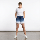 Woman wearing a white t-shirt and blue ombre shorts on a plain background