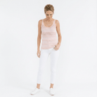 Woman wearing a pink lace tank top and white pants on a white background