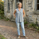 Woman standing in front of a stone building wearing a sleeveless floral top and light blue jeans.