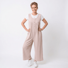 Woman wearing a beige jumpsuit with a white shirt underneath on a white background