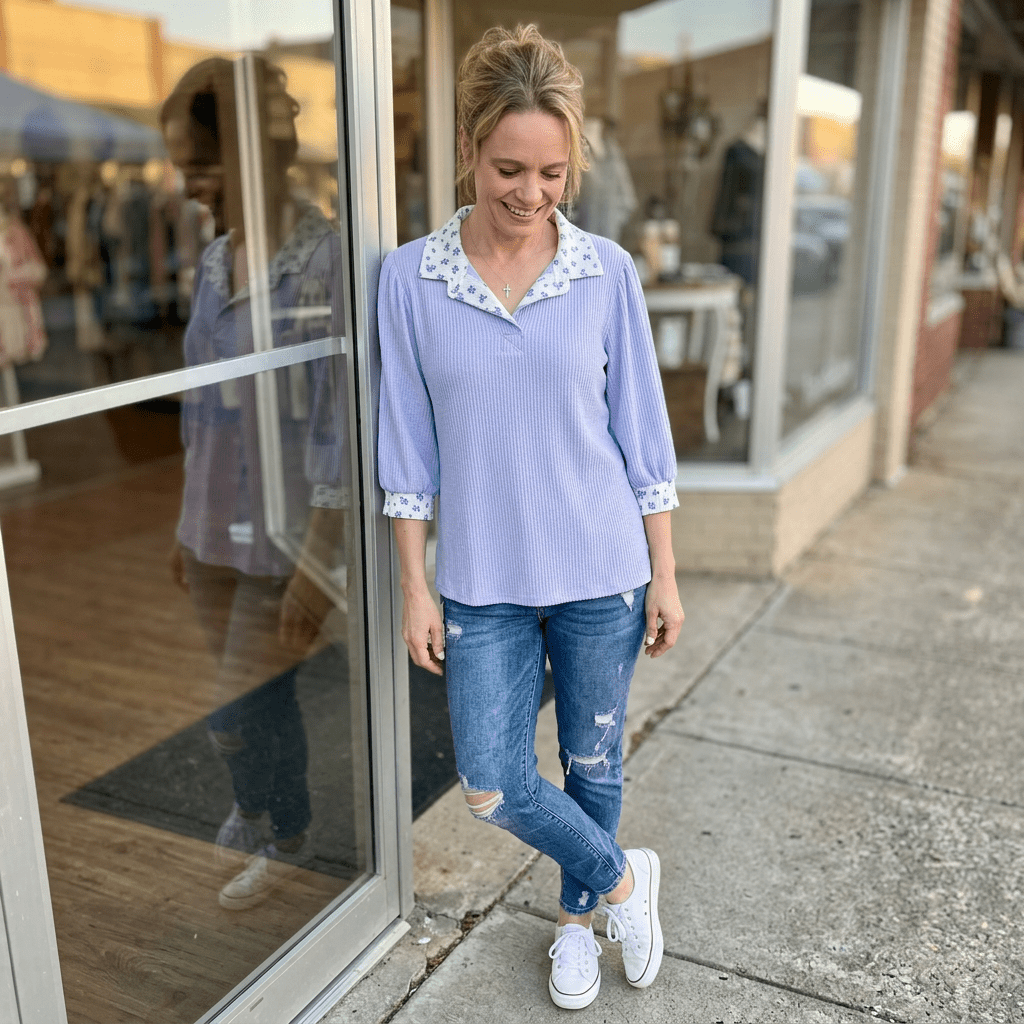 Woman wearing a light blue blouse with floral collar and ripped jeans standing outside a store.