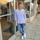 Woman wearing a light blue blouse with floral collar and ripped jeans standing outside a store.
