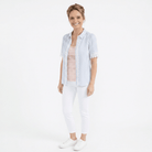 Woman wearing a light blue striped shirt and white pants on a white background