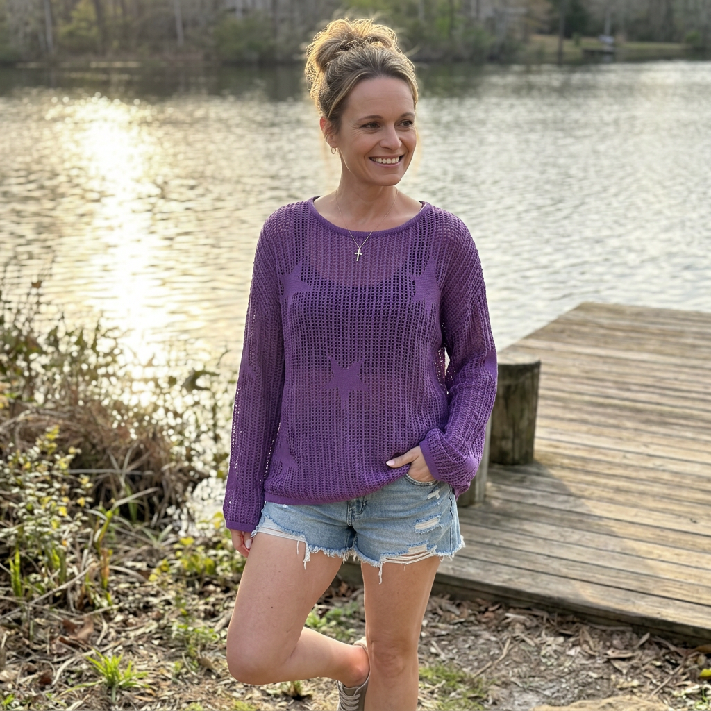 woman standing by a lake wearing a purple star pattern crochet long sleeve top.