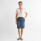 Woman wearing a white shirt with pink accents and a blue denim skirt on a white background